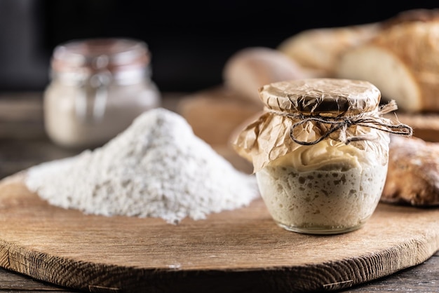 Levain de seigle mûri dans un bocal avec de la farine sur une planche à découper