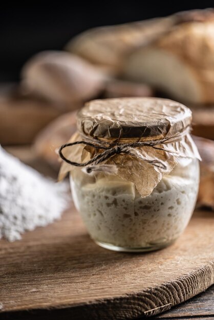 Levain de seigle mûri dans un bocal avec de la farine sur une planche à découper