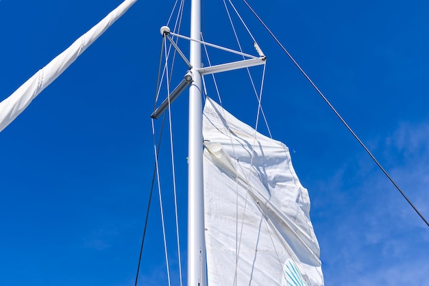 Levant la voile sur un yacht Captan jeune homme soulevant la voile du yacht catamaran pendant la croisière yacht à voile de luxe avec des voiles relevées par le gréement