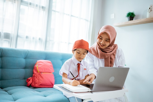 Élève du primaire musulman asiatique avec sa mère assise à faire ses devoirs à la maison