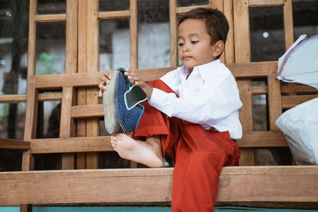 Élève de l'école primaire indonésienne se prépare à l'école le matin, attachant des chaussures devant la maison