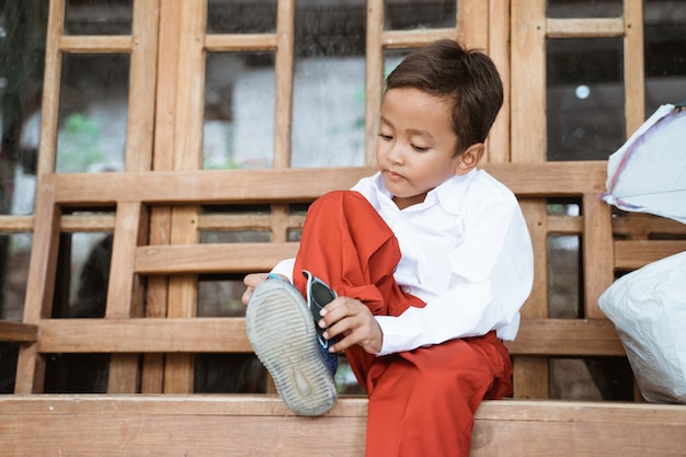 Élève de l'école primaire indonésienne se prépare à l'école le matin, attachant des chaussures devant la maison