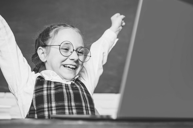 Élève Excidet Petit étudiant assis à table et écrit sur un ordinateur portable Drôle de petit enfant pointant vers le haut o