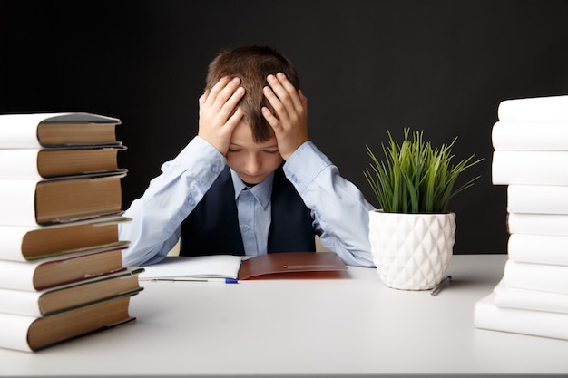 Élève de garçon triste avec maux de tête. Enfant assis à la table et faire ses devoirs.