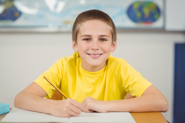 Élève souriant travaillant à son bureau dans une salle de classe