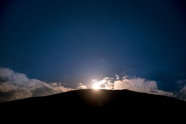 Levée de la pleine lune au-dessus de la montagne au ciel nocturne bleu foncé avec des étoiles