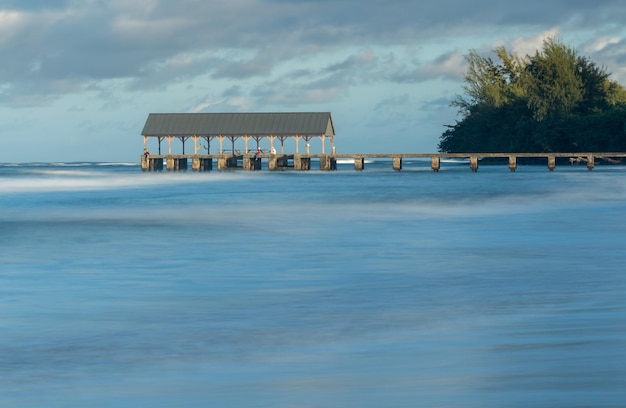 Le lever du soleil éclaire le ciel de l'aube au-dessus de la jetée d'Hanalei avec une exposition de longue durée aux vagues floues près d'Hanalei Kauai Hawaii