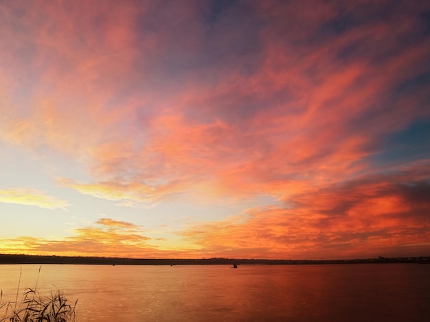 Lever du soleil sur le lac avec des roseaux au premier plan des nuages rouge orange