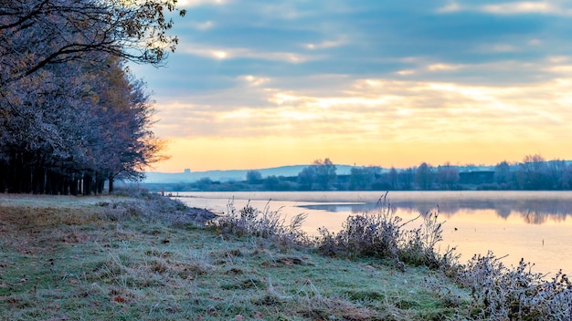 Photo lever du soleil sur la rivière un matin glacial. arbres et herbe couverts de givre au bord de la rivière le matin