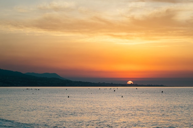 Lever de soleil matinal orange coloré sur l'océan Silhouettes de surfeurs dans des vagues de mer calmes contre un ciel nuageux peint en orange vif Les premiers rayons de soleil se reflètent sur la surface de l'eau