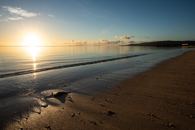 Lever de soleil serein à l'horizon, sable doré illuminé par la lumière du soleil. L'île d'Iriomote.