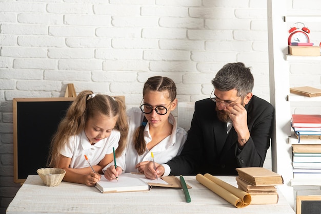 Élèves du primaire avec enseignant en classe Père enseignant aux écolières Père et petites filles à l'école Lecture de livre et écriture