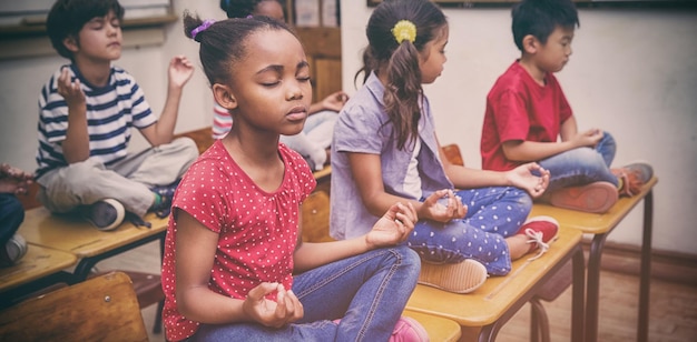 Élèves méditant en position du lotus sur un bureau dans une salle de classe à l'école primaire