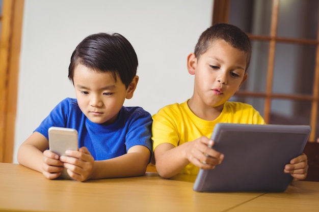 Élèves mignons en classe en utilisant le téléphone et la tablette