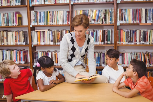 Élèves mignons et enseignant lisant dans la bibliothèque