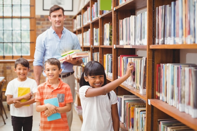 Élèves mignons et enseignant à la recherche de livres dans la bibliothèque