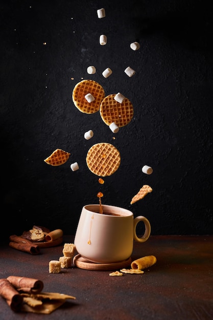 Lévitation de biscuits et de guimauves avec et éclaboussures dans une tasse sur fond sombre.