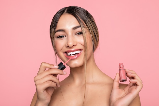 Lèvres de femme sexy avec maquillage rose et brillant, gros plan d'une jeune femme à la peau foncée appliquant un brillant à lèvres avec un pinceau sur fond blanc