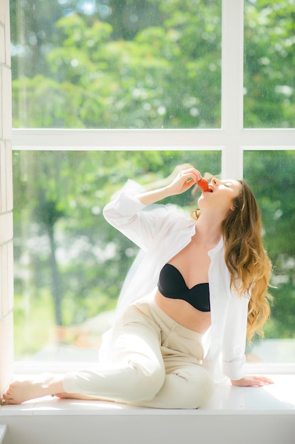 Lèvres de fraise Belle jeune femme torse nu tenant une fraise dans sa main et dégustation