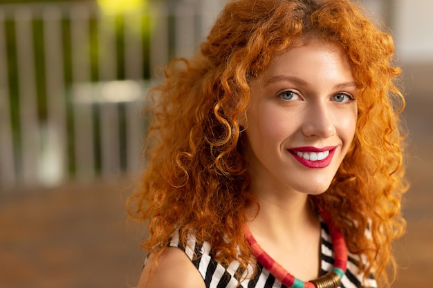 Lèvres roses. Belle femme bouclée aux cheveux roux avec des lèvres roses souriant largement tout en se sentant bien