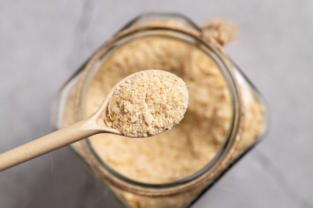 Levure nutritionnelle en flocons avec une cuillère en bois et un bocal en verre sur fond gris