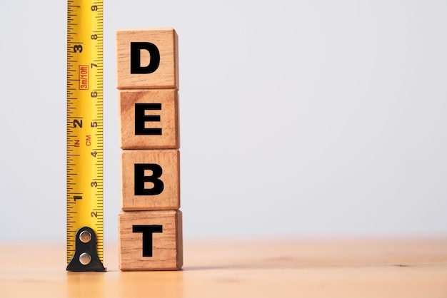 Libellé de la dette empilant sur un cube en bois avec ruban de mesure jaune pour le concept d'analyse de la dette