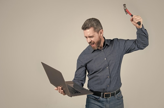 Libérer la colère sur l'ordinateur Homme stressé criant et cassant un ordinateur portable avec un marteau