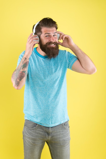 La liberté sans fil vous offre une inégalée Hipster heureux d'utiliser des écouteurs sans fil modernes Casque sans fil conçu pour offrir un son clair Homme barbu écoutant de la musique gadget sans fil