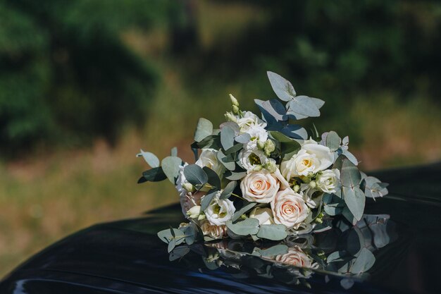 Libre d'un bouquet de mariage de roses crème avec des feuilles vertes se trouve sur une voiture noire