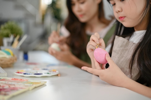 Libre de droit Une adorable jeune fille asiatique se concentre sur la peinture d'un œuf de Pâques à l'aquarelle