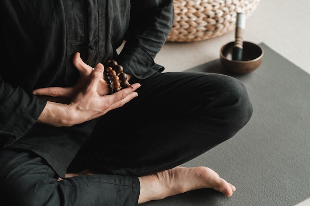 Libre d'un homme dans un kimono noir assis en position du lotus sur un tapis de gym à l'intérieur