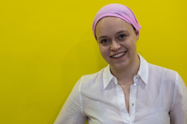 Libre d'une jeune femme souriante portant un foulard rose en référence au cancer sur fond jaune