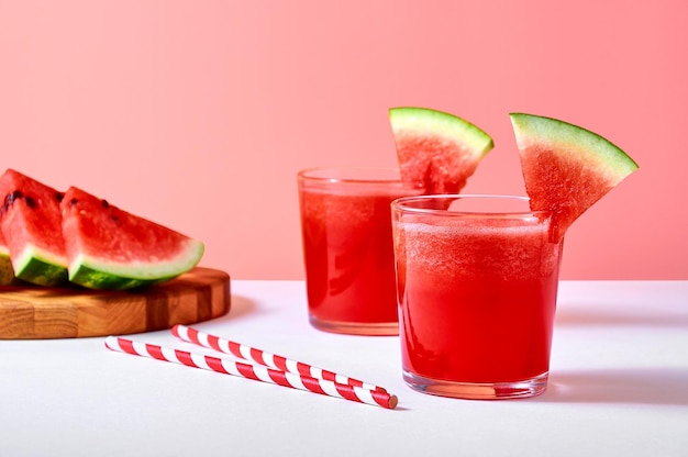 Libre de jus de pastèque frais ou smoothie dans des verres avec des morceaux de pastèque sur fond rose