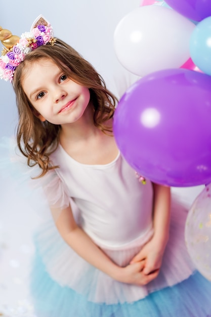 Licorne fille posant près de ballons à air chaud. Idée pour décorer une fête d'anniversaire de style licorne. Décoration de licorne pour fille de fête