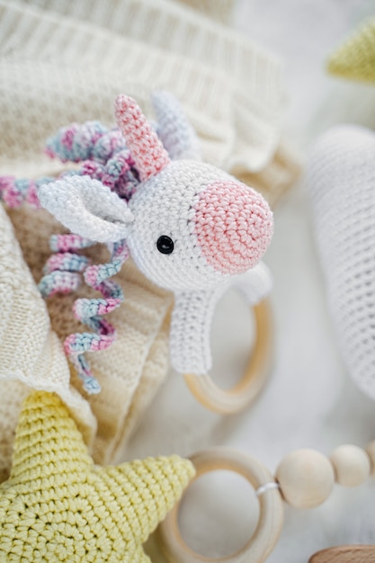 Photo licorne jouet tricoté et anneau de dentition en bois pour nouveau-né sur lit blanc. articles et accessoires pour bébé.