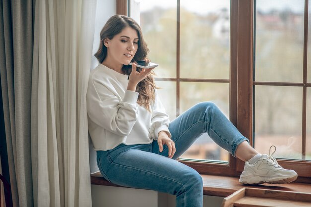 Lié. Jeune femme en blouse blanche et jeans avec un smartphone