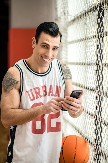Lié. Jeune sportif avec tatoo tenant un smartphone dans ses mains