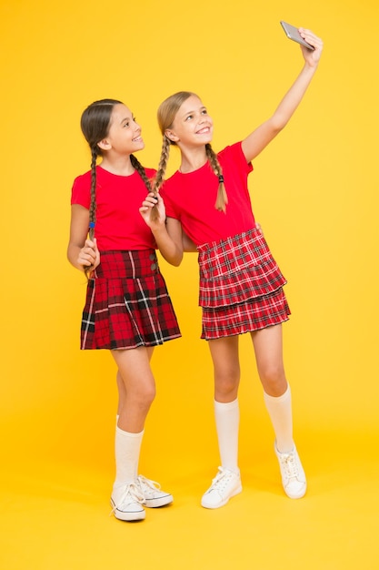 Liens familiaux fraternité et amitié heureuse journée de la connaissance bonheur de l'enfance concept d'éducation retour à l'école réseau social filles en uniforme petites filles font selfie au téléphone en s'amusant