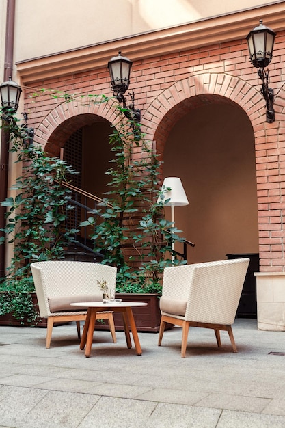 Un lieu de détente avec fauteuils en paille et torchère dans la cour sur fond d'arches en briques