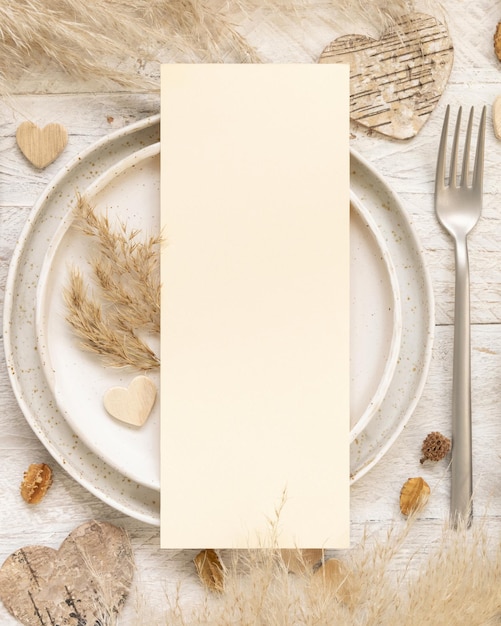 Lieu de table de mariage avec carte de menu vierge près de plantes séchées, feuilles de palmier, herbe de pampa et vue de dessus de coeurs. Scène Boho avec mise à plat de la carte papier verticale. Maquette de la Saint-Valentin