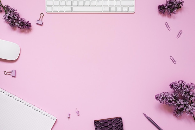 Lieu de travail avec bloc-notes stylo clavier souris papeterie et fleurs lilas sur fond rose avec espace de copie Mise à plat pour un blogueur