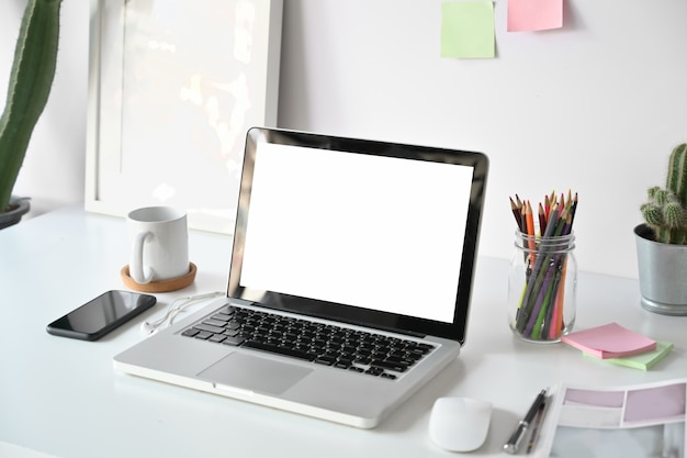 Lieu de travail confortable au bureau avec un ordinateur portable à écran blanc sur une table en bois blanche