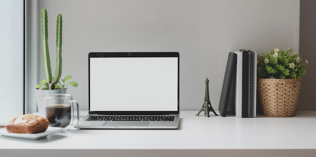 Lieu de travail confortable près des fenêtres avec ordinateur portable à écran blanc ouvert avec une tasse de café