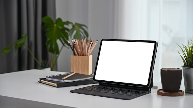 Lieu de travail confortable avec tablette informatique, ordinateur portable, tasse à café et plante sur un bureau blanc.