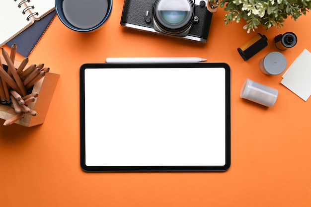 Lieu de travail créatif avec tablette numérique, appareil photo, tasse à café et ordinateur portable sur fond orange.