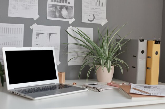 Lieu de travail à la maison ou au bureau avec un ordinateur portable de table avec des notes de dossiers de papier de fleur d'affichage vides sur le mur