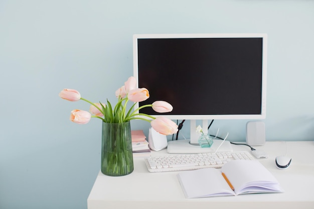 Lieu de travail moderne dans une pièce lumineuse aux murs bleus Bouquet de tulipes roses sur la table Espace de travail féminin