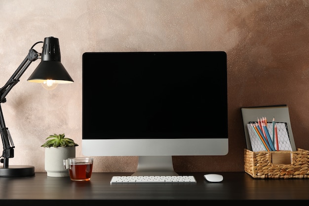 Lieu de travail avec ordinateur, plante et lampe sur table en bois.