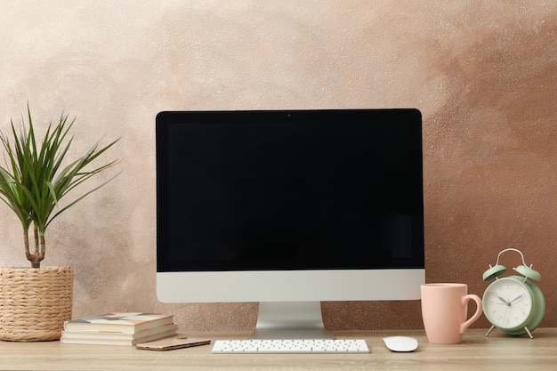 Lieu de travail avec ordinateur, plante et réveil sur table en bois.