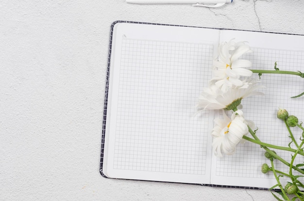 Lieu de travail plat avec bouquet de marguerites fraîches avec cahier vide